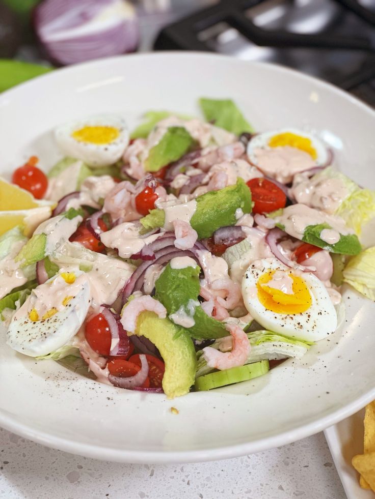 a salad with hard boiled eggs, tomatoes, onions and lettuce on a white plate