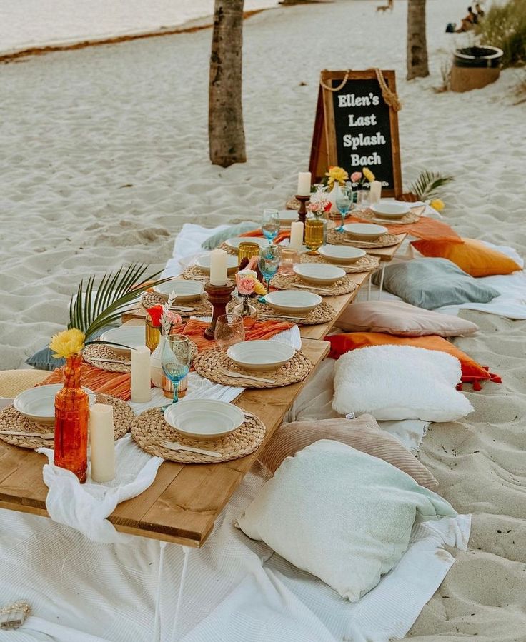 a long table set up on the beach for a picnic with candles, plates and napkins