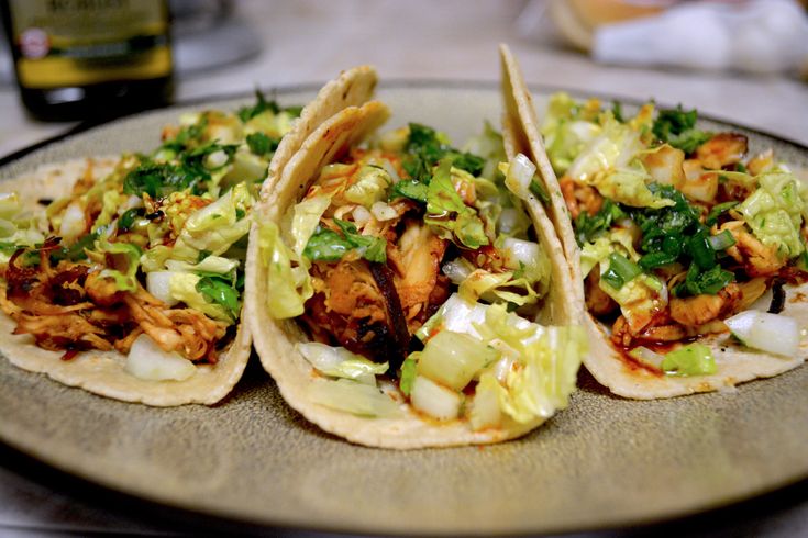 three tacos are sitting on a plate with coleslaw and chicken in them