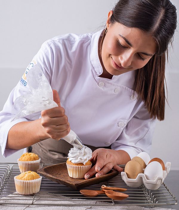 a female chef decorating cupcakes with icing on a tray and baking utensils