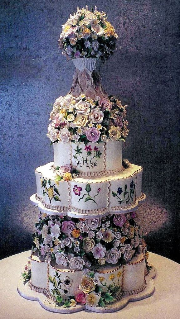 a three tiered wedding cake with flowers on it's sides and an elaborate topper