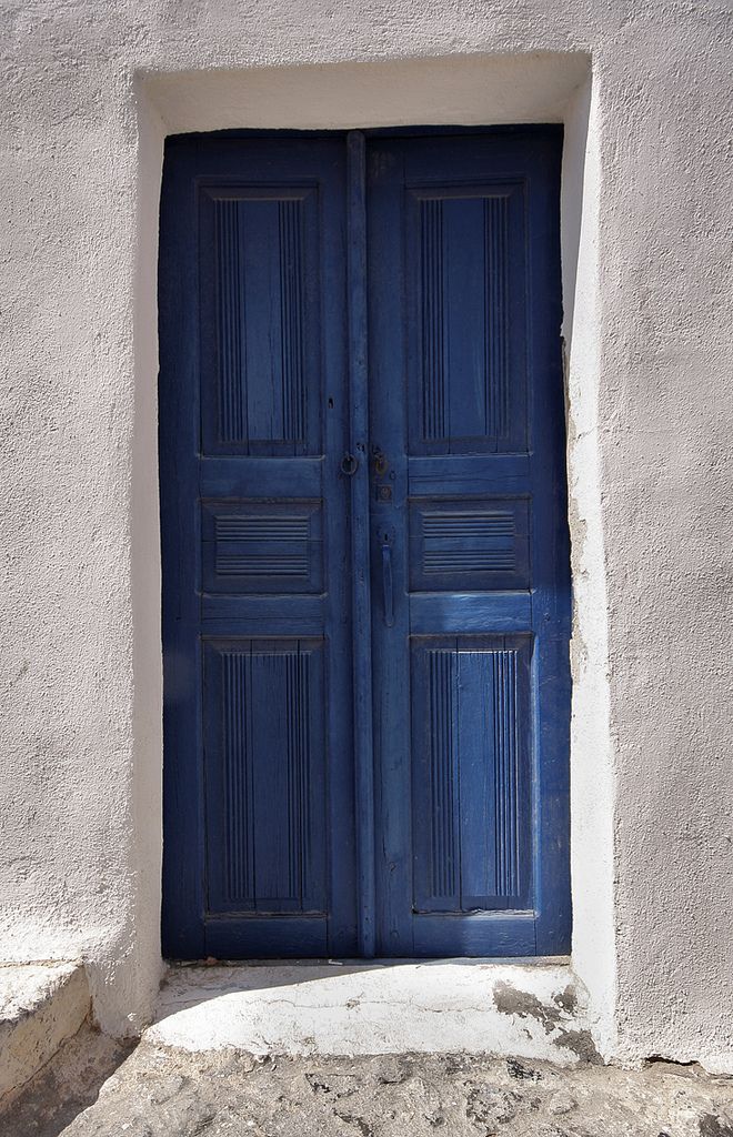 an open blue door on the side of a white building with stone steps leading up to it