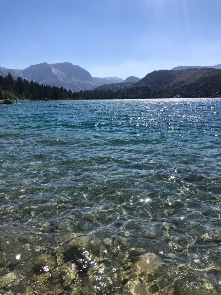 clear water with mountains in the background and sun shining on the water's surface