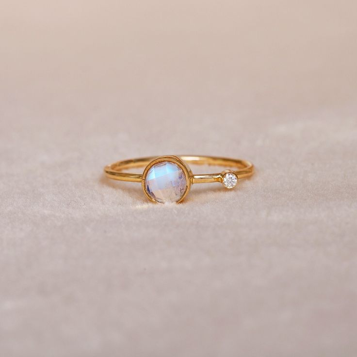 a gold ring with an opal and two diamonds on the side, sitting on a white surface