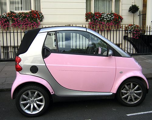 a pink and silver smart car parked in front of a building