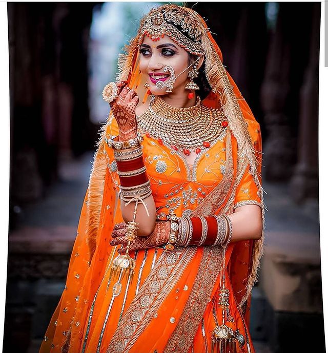 a woman dressed in an orange bridal outfit with jewelry and makeup on her face