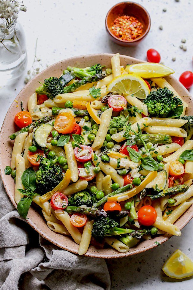 a bowl filled with pasta, broccoli and tomatoes next to some lemon wedges