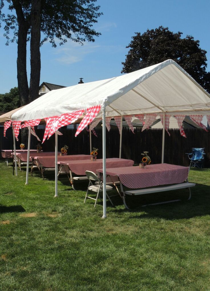 a tent with tables and chairs under it on the grass in front of some trees