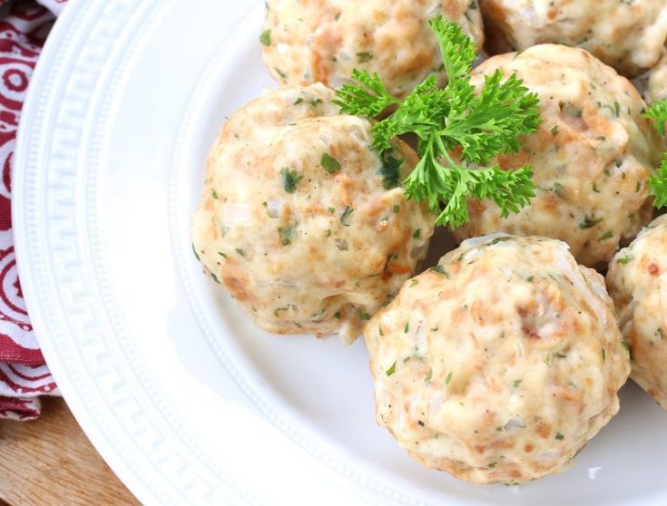 a white plate topped with meatballs covered in cheese and parsley on top of a wooden table