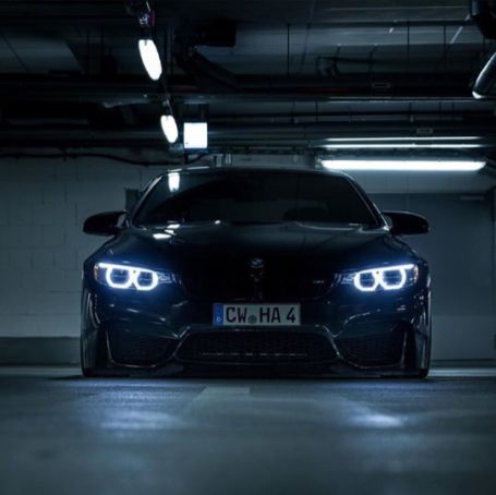 the front end of a black sports car in a parking garage at night with lights on