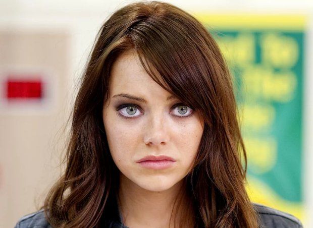 a woman with long brown hair and blue eyes looks at the camera while standing in front of a sign