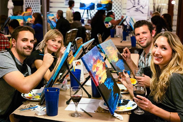 four people sitting at a table with paintings on it and drinks in front of them