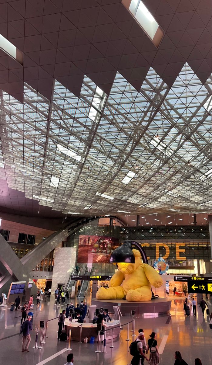 people are walking around in an airport with large yellow objects hanging from the ceiling above them