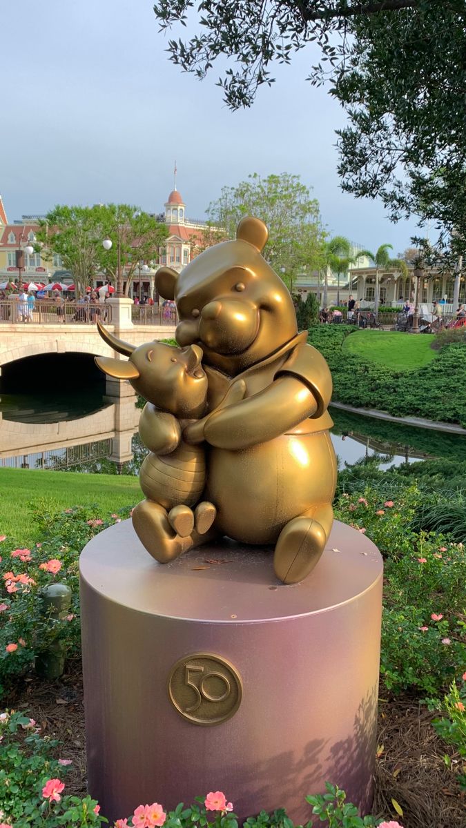 a statue of two bears hugging each other in front of a pond and bridge with pink flowers around it