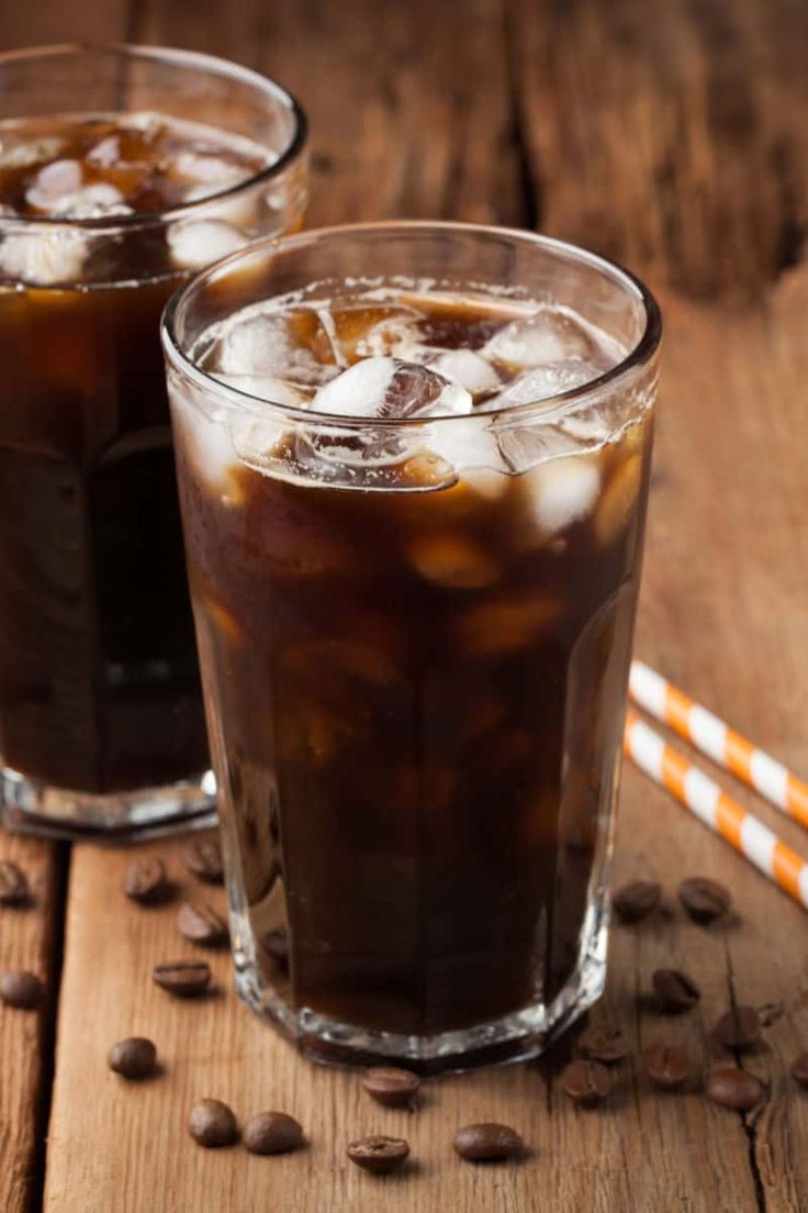 two glasses filled with iced coffee on top of a wooden table