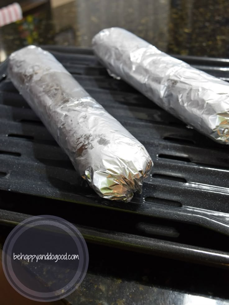 two silver foil wrapped burritos sitting on top of a black grill grate