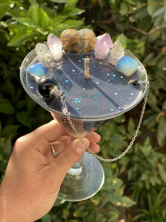 a person holding up a wine glass with rocks and beads on it in front of some bushes