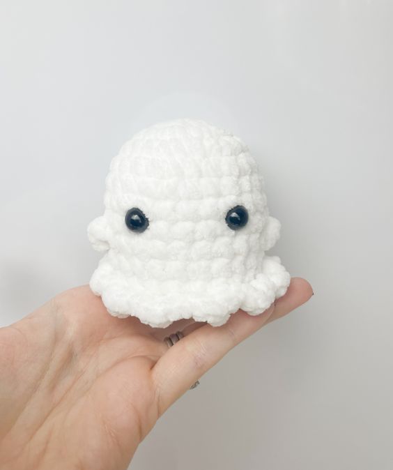 a hand holding a small white crocheted object with eyes on it's face