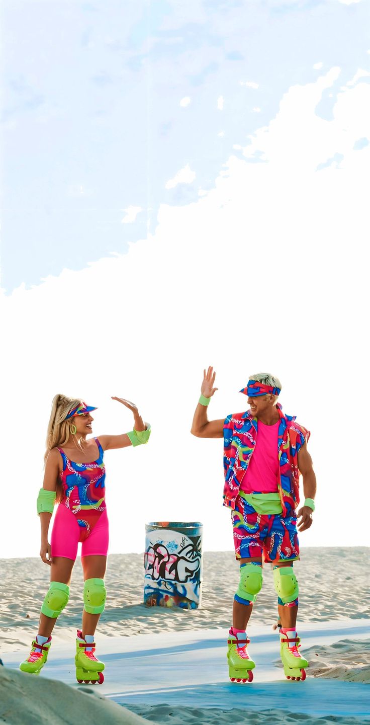 two people dressed in colorful clothing and roller skates standing on the beach with their arms outstretched