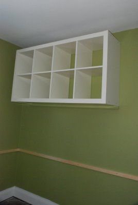 the empty room is painted green with white shelving units on each wall and wood flooring