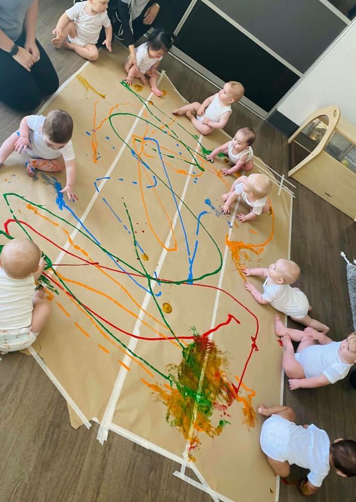 a group of children sitting around a table covered in paper and colored paint on it