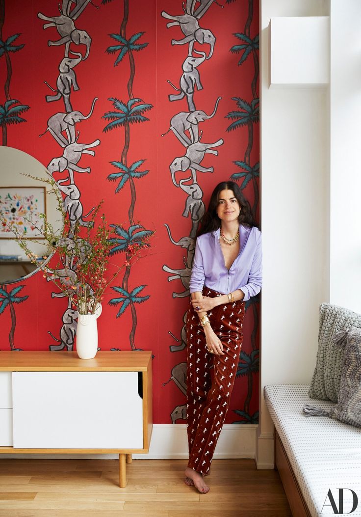 a woman standing in front of a red wallpapered room with an animal pattern