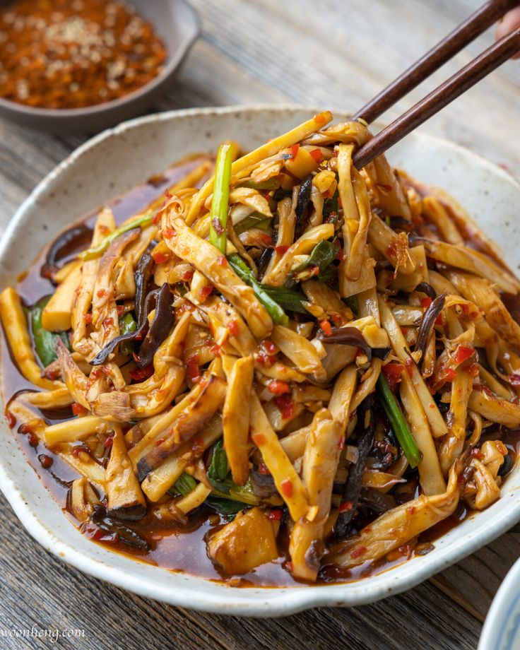 a white bowl filled with stir fry noodles and chopsticks on top of a wooden table