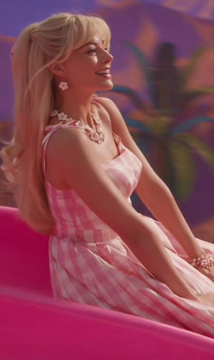 a woman sitting on top of a pink couch wearing a dress and pearls in her hair