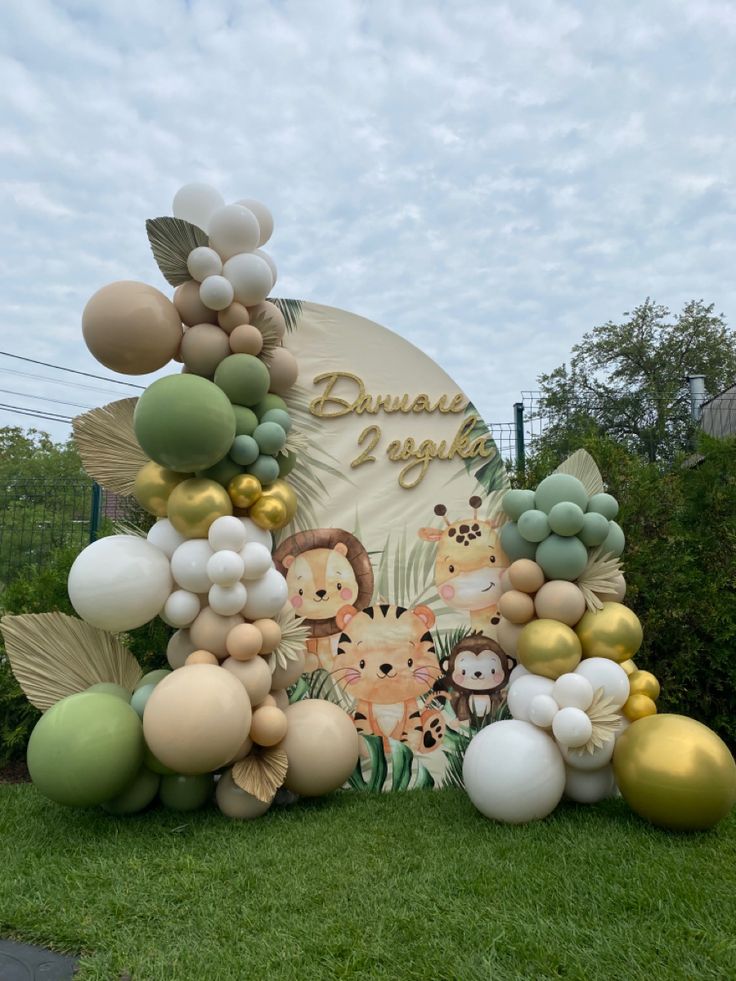 an outdoor display with balloons and jungle animals on the grass, surrounded by greenery