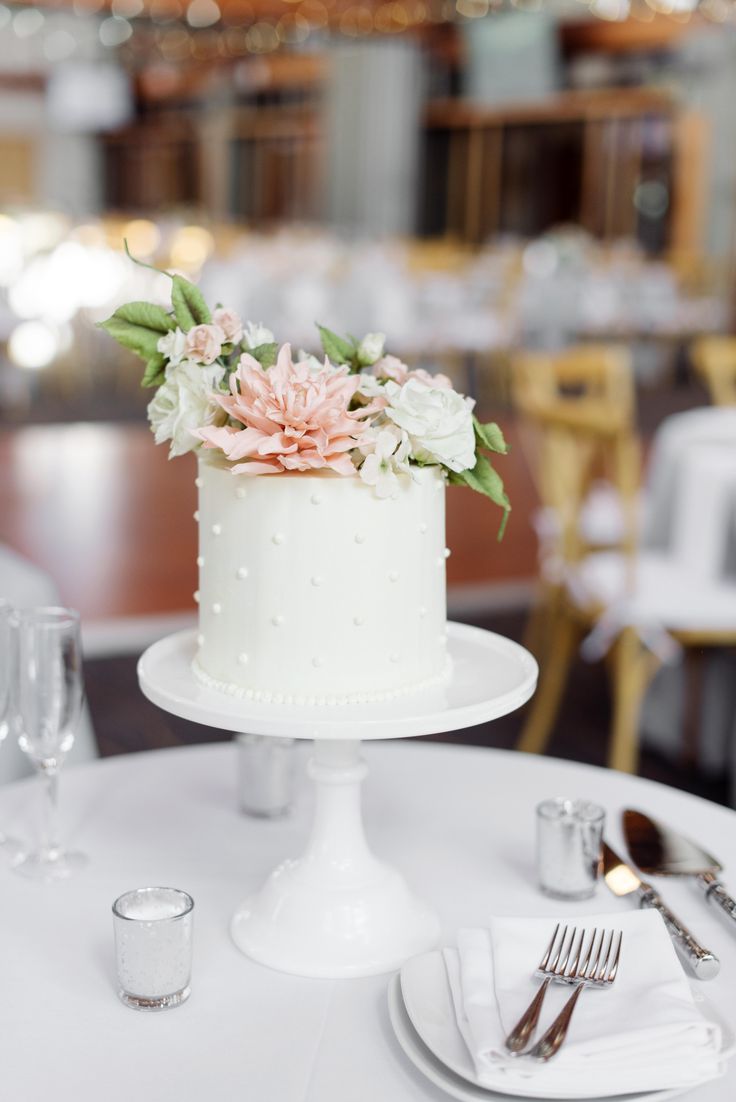 a white cake with pink flowers on top sitting on a table next to silverware