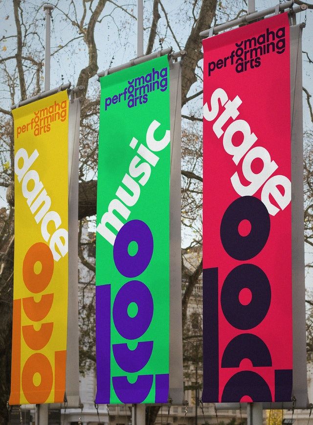 three colorful banners are hanging on poles in front of a building with trees behind them