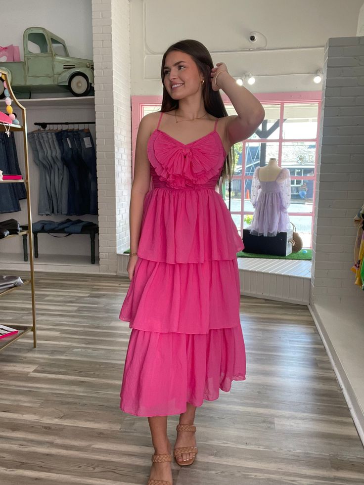 Let Elane's playful pleats charm you to sway with tiered ruffles! Don't miss the chance to twirl and whirl around in a flirty fuchsia that goes perfectly with a cheeky bow in front! Pink Tiered Dress For Garden Party, Pink Flowy Tiered Dress For Garden Party, Pink Tiered Dress With Ruffle Hem, Spring Pink Tiered Dress For Garden Party, Pink Tiered Ruffle Dress For Garden Party, Pink Tiered Dress For Spring Garden Party, Spring Garden Party Pink Tiered Dress, Pink Tiered Ruffle Dress With Layered Hem, Pink Tiered Dress With Ruffled Skirt And Straps