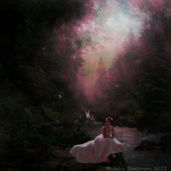 a woman in a white dress is sitting on rocks near a stream with trees and flowers