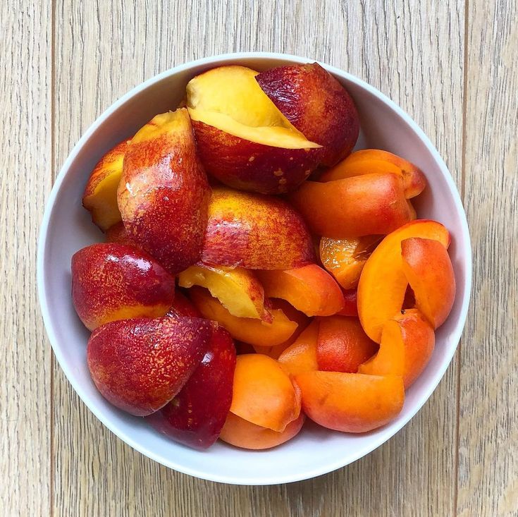 a white bowl filled with sliced peaches on top of a wooden table next to a knife