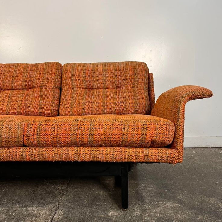 an orange and black couch sitting on top of a cement floor next to a white wall