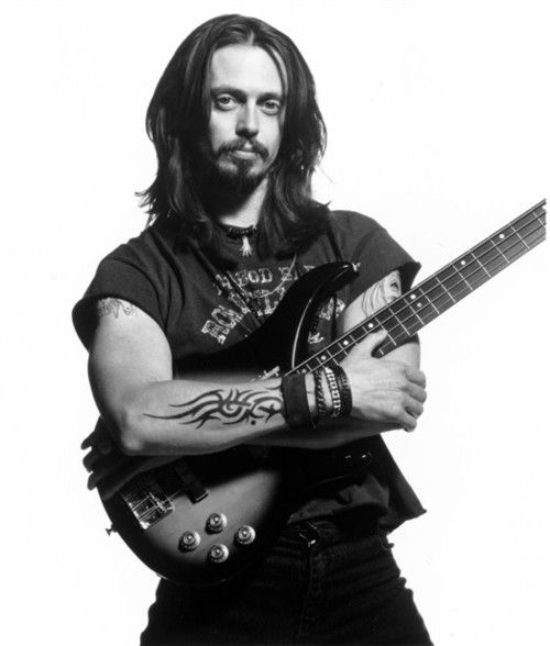 a man with long hair is holding a guitar and posing for a photo in front of a white background