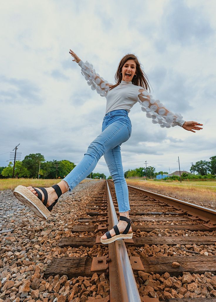 a woman is standing on a train track with her arms out and legs spread wide