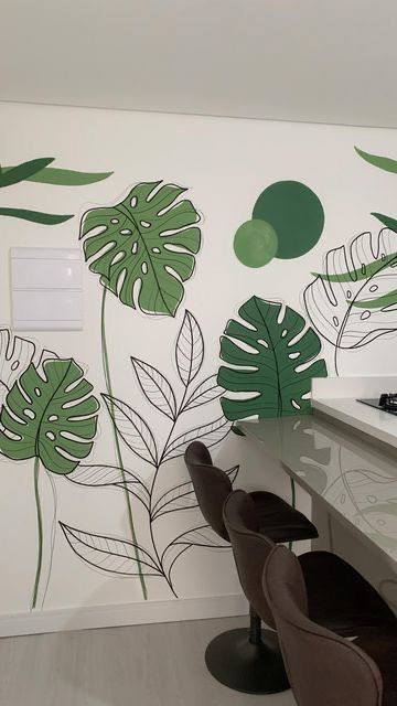 a kitchen with green leaves painted on the wall next to chairs and a stove top oven