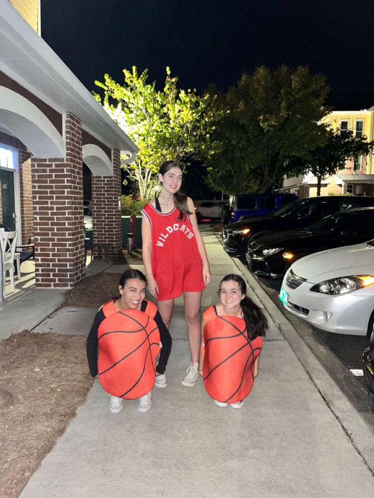 three girls in basketball uniforms standing on the sidewalk