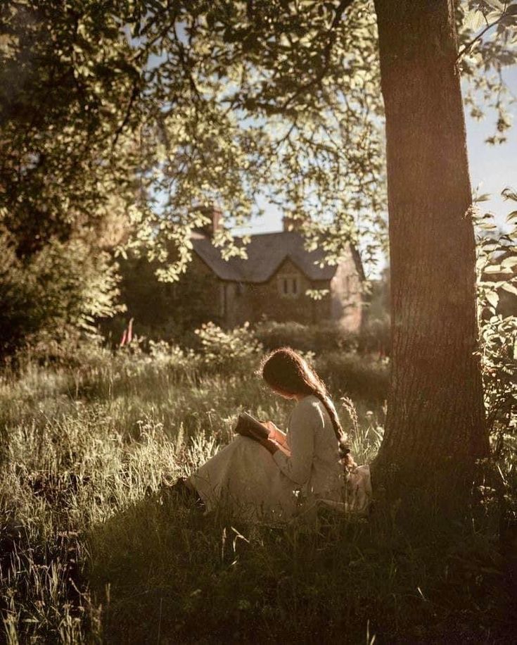 a woman sitting in the grass under a tree with her back to the camera,