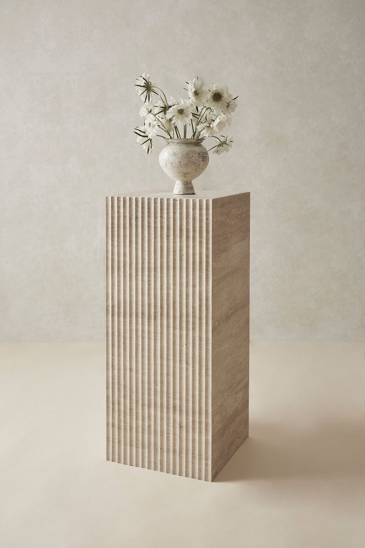 a vase with flowers in it sitting on top of a wooden block next to a wall