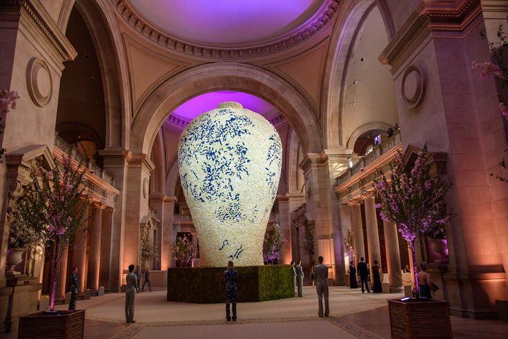 a large vase sitting in the middle of a room filled with plants and people standing around it