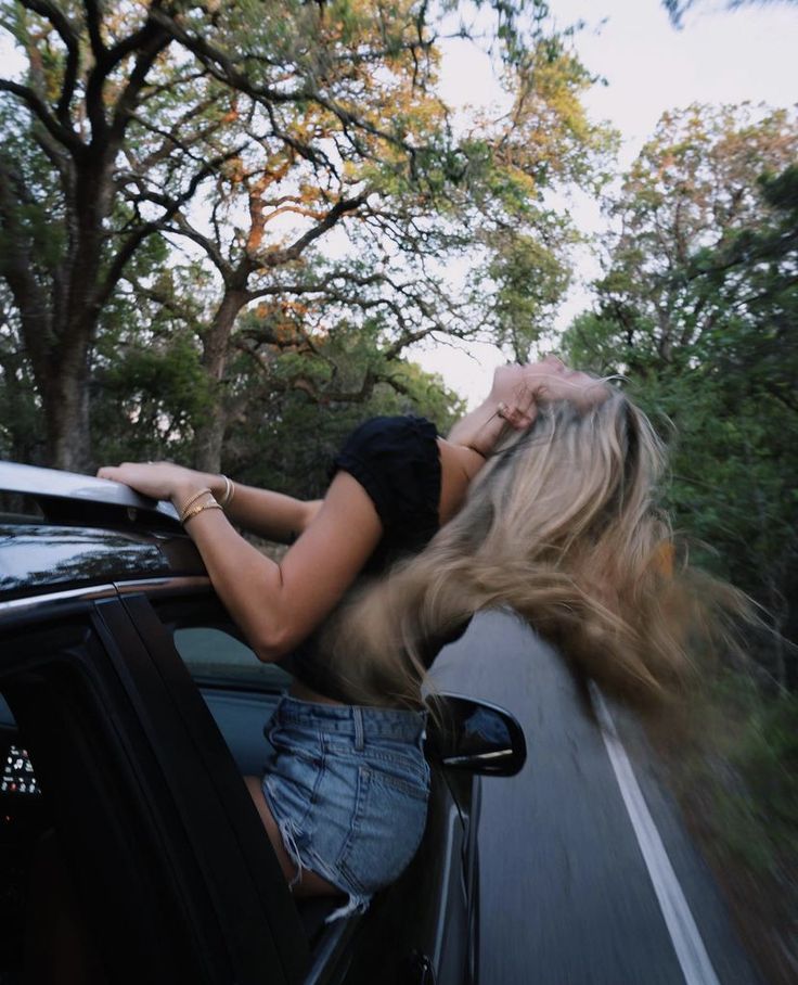 a woman leaning out the window of a car with her hair blowing in the wind