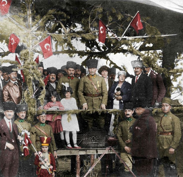 a group of people standing next to each other in front of trees and flags on poles