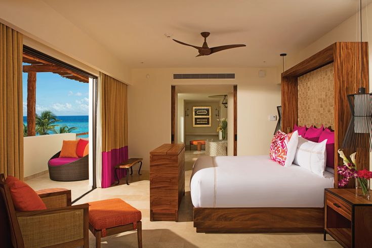 a bedroom with a large bed sitting next to a window covered in pink and orange pillows