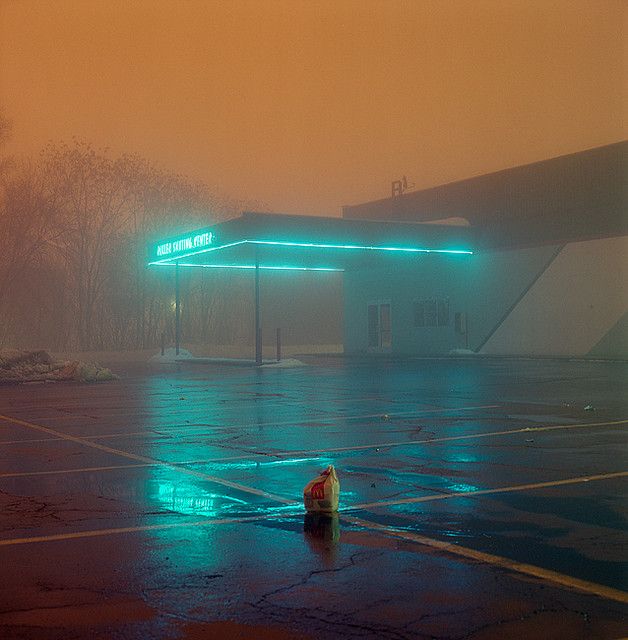 an empty parking lot with a gas station in the background on a foggy day