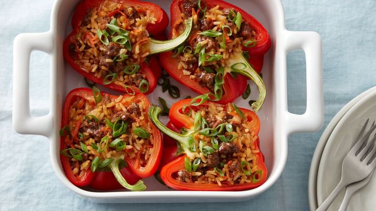 stuffed bell peppers in a white casserole dish next to a fork and knife