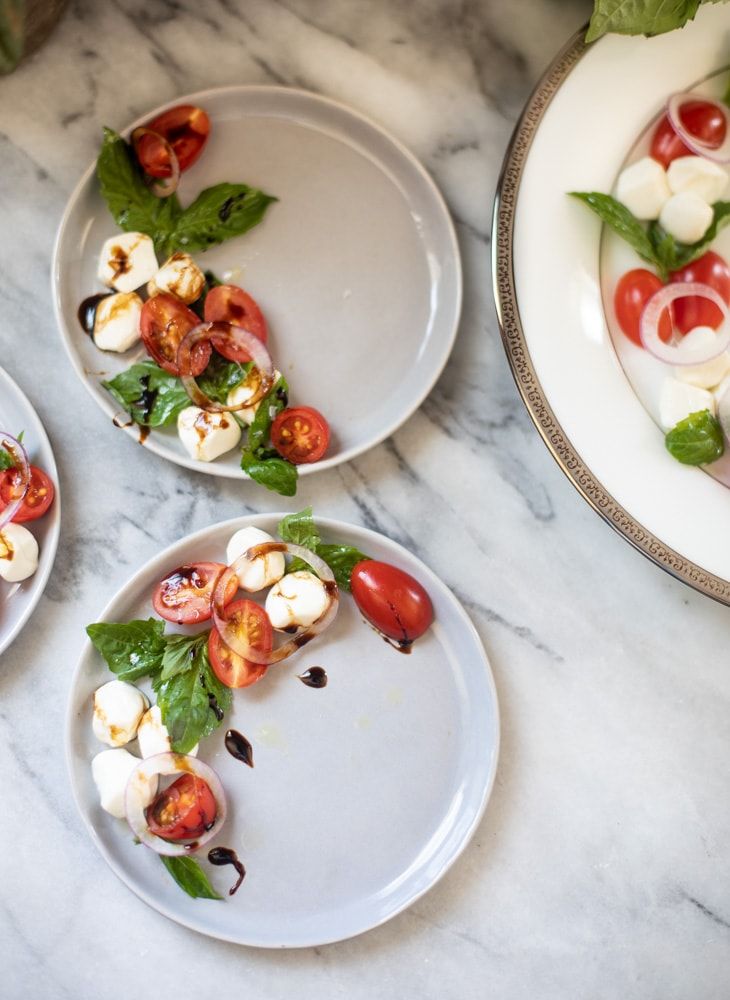 three plates with tomatoes, mozzarella and basil on them sitting on a marble table