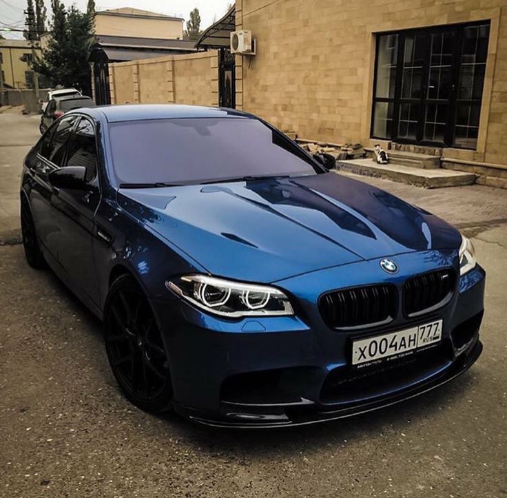 a blue bmw is parked in front of a brick building on the side of the road