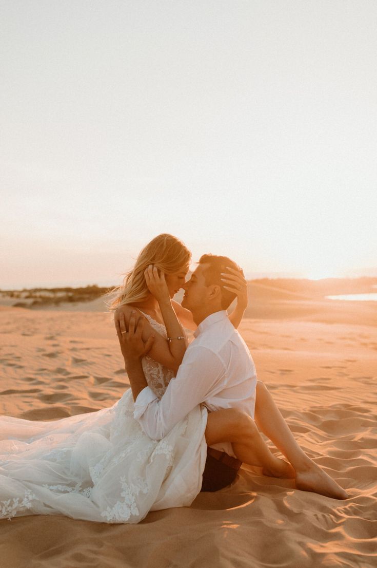 a man and woman are sitting on the sand in the desert, kissing each other